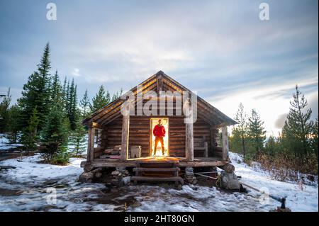 Maschio in piedi nella porta di Snow Peak Cabin nella foresta nazionale Foto Stock