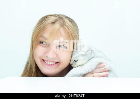 Donna bionda adulta che tiene un gatto inglese d'argento. Amicizia di un essere umano con un animale domestico. Foto Stock