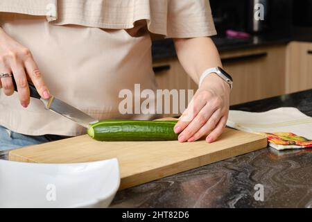 Donna incinta irriconoscibile in cucina taglio fresco e succosa cetriolo per insalata Foto Stock