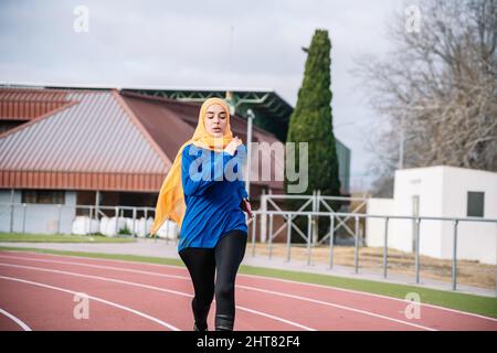 Sportivo etnico attivo in hijab che corre su pista Foto Stock