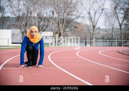 Donna etnica seria in pronta posizione sulla pista di corsa Foto Stock