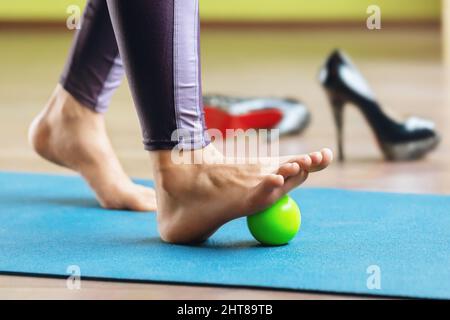 Rilassamento miofasciale dei muscoli ipermobili del piede con una palla da massaggio, in piedi su un tappetino in studio. Prevenzione dell'affaticamento delle gambe dopo lo svezzamento Foto Stock