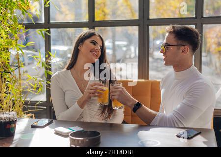 Gli amici socializzano, si divertono e ridono bevendo caffè nella caffetteria mentre si imbrogliano. Amici di sesso maschile e femminile che scattano foto insieme Foto Stock