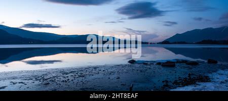 Il tramonto d'inverno getta un bagliore su un'acqua ghiacciata di Derwent e sulle montagne del Lake District d'Inghilterra. Foto Stock