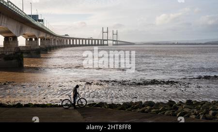 Un ciclista si ferma sul sentiero lungomare di Severn Beach, con il secondo ponte Severn Crossing alle spalle. Foto Stock