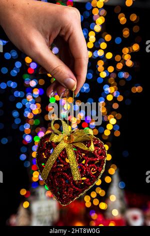 Colpo verticale di una mano che tiene ornamento a forma di cuore contro sfondo bokeh Foto Stock