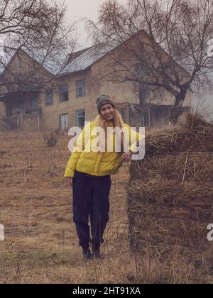 Una donna sorridente si erge sul pagliaio sullo sfondo di un vecchio edificio abbandonato in una mistica torbida torbida. Messa a fuoco soft. Foto Stock