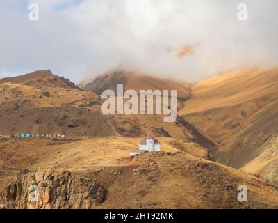 In alto tra le montagne, tra le nuvole scese fino alle cime vicino alla scogliera, sorge una casa bianca con finestre strette e tetto rosso. Foto Stock