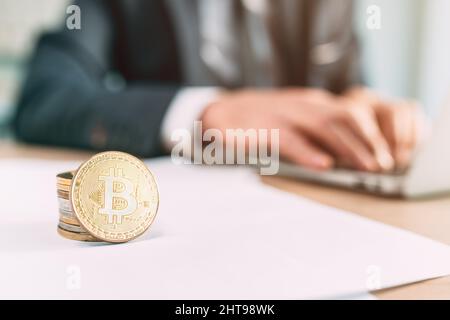 Bitcoin Cryptocurrency trader concetto, primo piano di monete impilate su ufficio scrivania e uomo d'affari utilizzando computer portatile in background Foto Stock