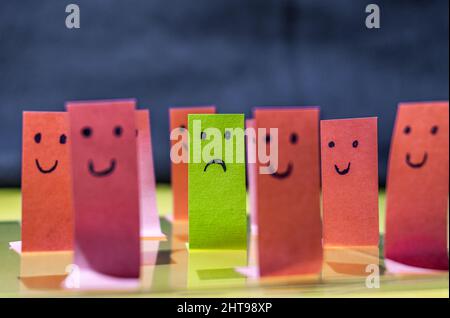 Faccia triste su un adesivo verde circondato da volti sorridenti su adesivi rosa Foto Stock