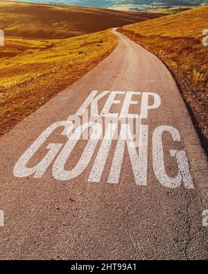 Continua a dare un messaggio motivazionale sulla strada asfaltata attraverso il paesaggio di campagna, fuoco selettivo Foto Stock