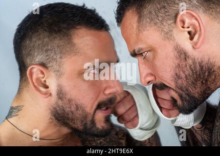 Uomo aggressivo arrabbiato. Il ritratto del hipster sembra brutale. Il ragazzo dispiaciuto sta guardando lo specchio. Frustrazione e pericolo. Foto Stock