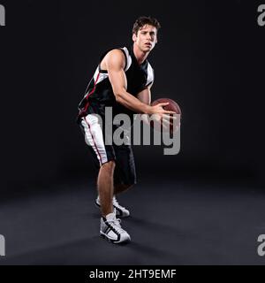 Vincere non è tutto, ma la volontà di vincere è. Full length studio girato di un giovane giocatore di basket maschile in azione su sfondo nero. Foto Stock