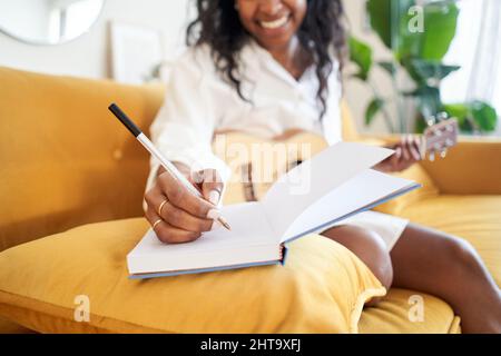 Primo piano della mano di una donna che scrive in un notebook. Nuove idee che ispirano cantante componendo musica con una chitarra a casa. Foto Stock