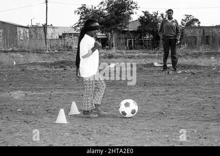 Scatto in scala di grigi dei giovani bambini africani che svolgono attività legate al calcio in un parco giochi scolastico Foto Stock