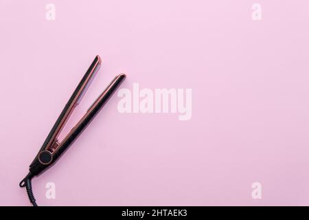 Vista dall'alto del ferro per lisciare i capelli neri su sfondo rosa. Concetto di cura dei capelli Foto Stock