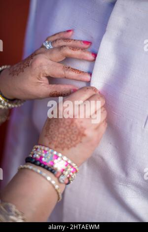 Colpo verticale di una donna con henné sulle sue mani che si abbottona su una camicia dello sposo per un matrimonio Foto Stock