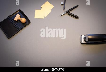 Vista dall'alto di un francobollo in legno con inchiostro, pinzatrice, note adesive e marcatori isolati su sfondo grigio Foto Stock