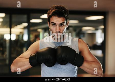 Concorrenza fortemente focalizzata. Ritratto di un uomo concentrato che indossa guanti da boxe e abbigliamento sportivo in posa per combattere in palestra. Foto Stock