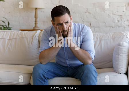 L'uomo seduto sul divano sembra depresso, pensando ai problemi Foto Stock