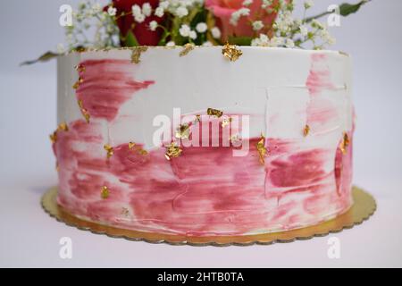 Foto di una torta bianca con decori di pennelli rosa e condimenti di rose Foto Stock