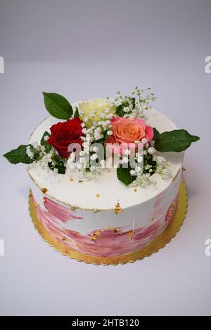 Foto di una torta bianca con decori di pennelli rosa e condimenti di rose Foto Stock