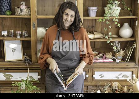 Caucasica donna fiorista leggere un giornale mentre in piedi nel suo negozio di fiori - concetto di donna d'affari Foto Stock