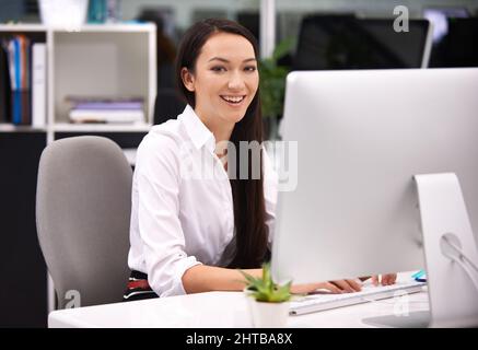 Divertirsi al lavoro. Ritratto di una giovane donna d'affari attraente che lavora alla sua scrivania. Foto Stock