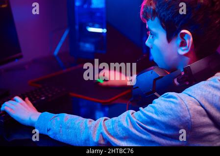 Ragazzo adolescente giocare video gioco computer in camera oscura, utilizzare tastiera meccanica rgb neon colorato, luogo di lavoro per il gioco di cybersport, giochi per bambini dipendenza Foto Stock