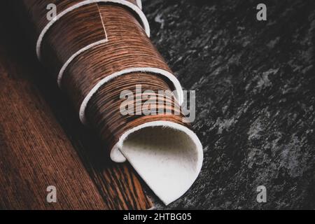 Linoleum. Rotolo di linoleum su sfondo nero. Rivestimenti per pavimenti. Posa di rivestimenti per pavimenti. Tessitura di legno su un rotolo. Il campione viene arrotolato. Foto Stock