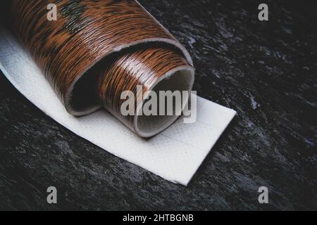 Linoleum. Rotolo di linoleum su sfondo nero. Rivestimenti per pavimenti. Posa di rivestimenti per pavimenti. Tessitura di legno su un rotolo. Il campione viene arrotolato. Foto Stock