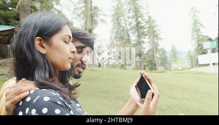 Poco profondo fuoco di una bella coppia del sud asiatico prendendo un selfie su un telefono in un parco Foto Stock