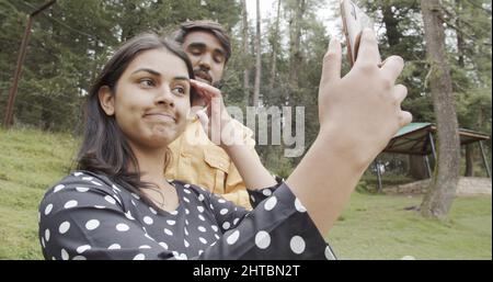 Poco profondo fuoco di una bella coppia del sud asiatico prendendo un selfie su un telefono in un parco Foto Stock