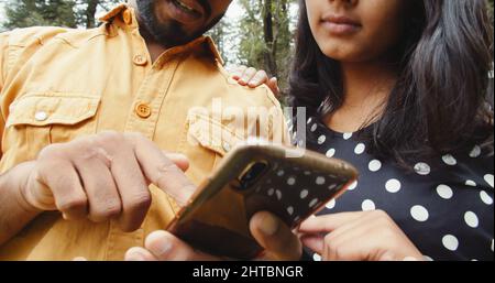 Shallow focus of a lovely South Asian young adult couple discussing a picture on the phone in a park Stock Photo