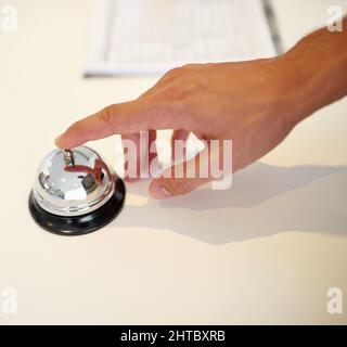 Squilla in vacanza. Scatto di una mano che suona un campanello al banco del check-in dell'hotel. Foto Stock