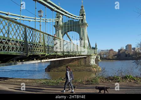 sulle rive del tamigi a barnes, due donne camminano un cane che sta per passare sotto il ponte hammersmith, londra, inghilterra Foto Stock