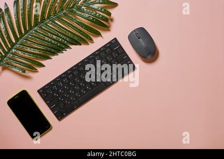 Vista dall'alto di una tastiera, un telefono e un mouse su sfondo rosa Foto Stock