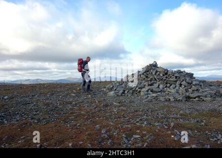Single Lone Man Walking al Summit pile of Stones (Cairn) della montagna scozzese Munro 'ben Chonzie' a Glen Lednock, Perthshire, Scozia, Regno Unito. Foto Stock