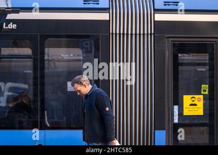 L'uomo passa davanti a un tram con una testa sospesa. Maschere obbligatorie sul treno a Monaco di Baviera, Germania Foto Stock