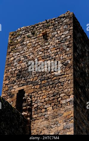 Macerie cortigiate si elevano su blocchi di pietra più lisci nelle fasi superiori della torre di avvistamento sopra la porta Romea o porta Franca, ingresso sud della rocca collinare di Monteriggioni, Toscana, Italia. La città fu fondata da Siena nel 1213 contro Firenze, il suo nemico amaro in guerre che durarono diversi secoli medievali. Foto Stock