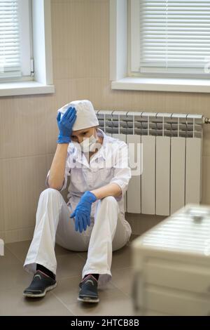 Una dottoressa siede stancamente sul pavimento dell'ospedale. Foto Stock