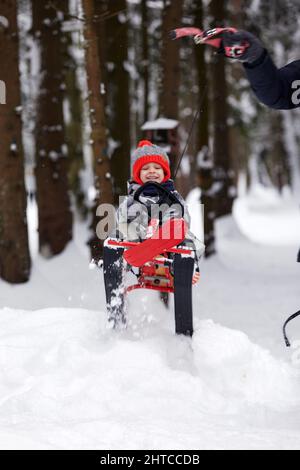 un ragazzo felice in discesa su una slitta in inverno, un bambino in abiti luminosi siede su una slitta, la neve lo vola Foto Stock