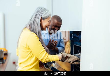 immagine cinematografica di una coppia anziana multietnica che prepara il cibo in cucina. Momenti di stile di vita in interni a casa. Concetto di anzianità e relazioni Foto Stock