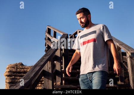 bel giovane uomo che cammina lungo una scala di legno con il cielo blu sullo sfondo, concetto di tempo libero e relax, spazio copia per il testo Foto Stock