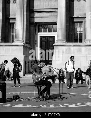 Scala di grigi verticale di un busker che gioca a "Wicked Game" di Chris Isaak al Trafalgar Square, Londra Foto Stock