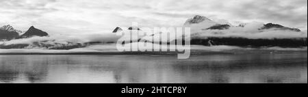 Foto panoramica di un lago circondato da colline rocciose coperte di nebbia e neve in campagna Foto Stock