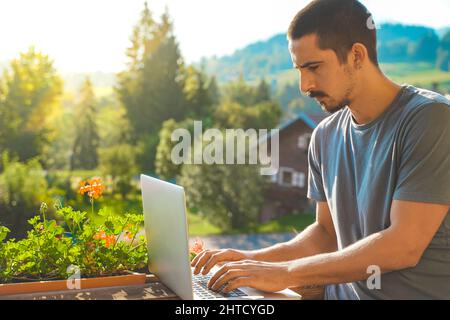 Giovane uomo d'affari che lavora con un computer portatile su uno splendido sfondo panoramico di montagna. Uomo attraente che lavora. Freelance. Viaggiatore. Foto Stock