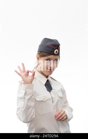 Bella giovane donna russa ufficiale di polizia in uniforme vestito mostra i segni della mano perfettamente e sorride su uno sfondo bianco. Messa a fuoco selettiva. Verticale Foto Stock