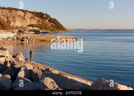 Uomo che pesca in un pomeriggio d'inverno nella baia di Sistiana, sulla costa vicino Trieste, Italia Foto Stock