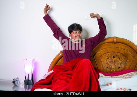 Il giovane si sveglia al mattino allungando le braccia in camera da letto - concetto di rinfresco, stile di vita sano e sonno confortevole Foto Stock